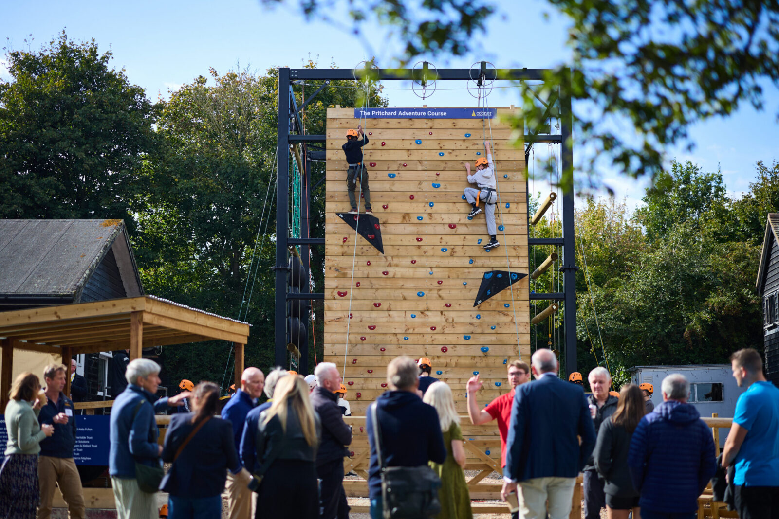 People enjoying a community climbing wall event outdoors with spectators and participants.